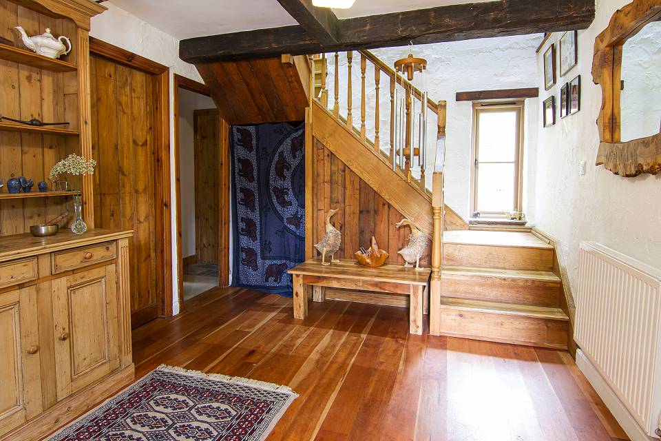 Hallway with wooden floor and rug, and wooden staircase winding upstairs