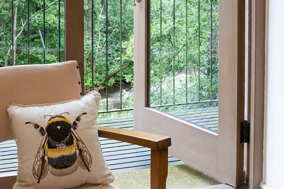 A close up of a chair with a bee cushion next to an open patio door with the river beyond