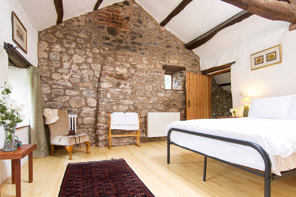 Bedroom with stone gable wall and exposed oak beams